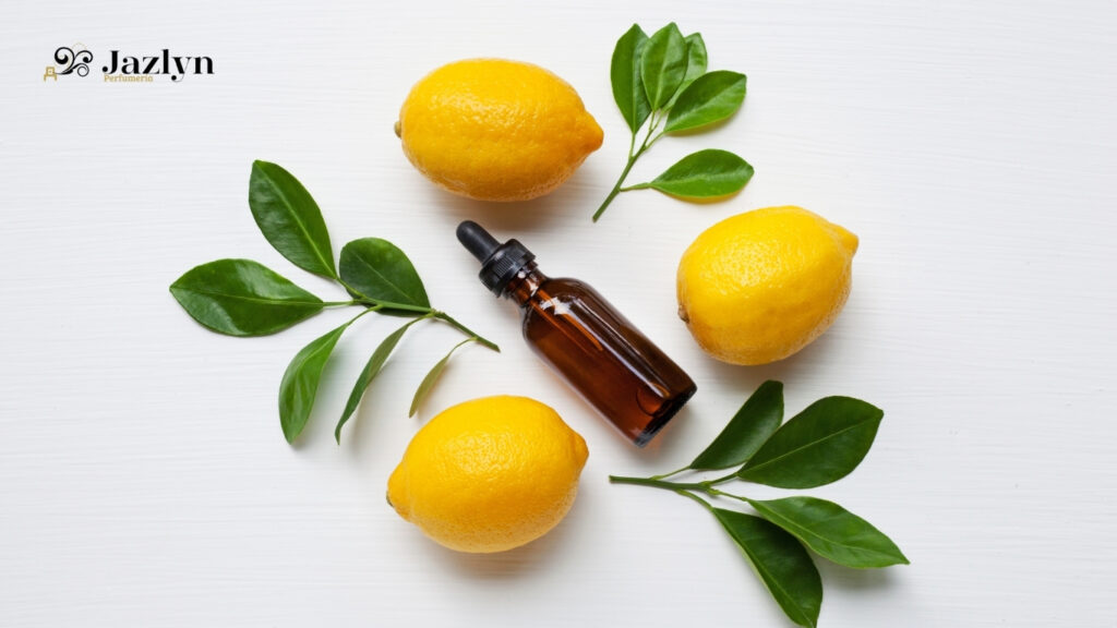 Frascos de aroma de limón a base de aceites esenciales junto a limones frescos y hojas verdes sobre fondo blanco. Producto de Jazlyn Perfumería.