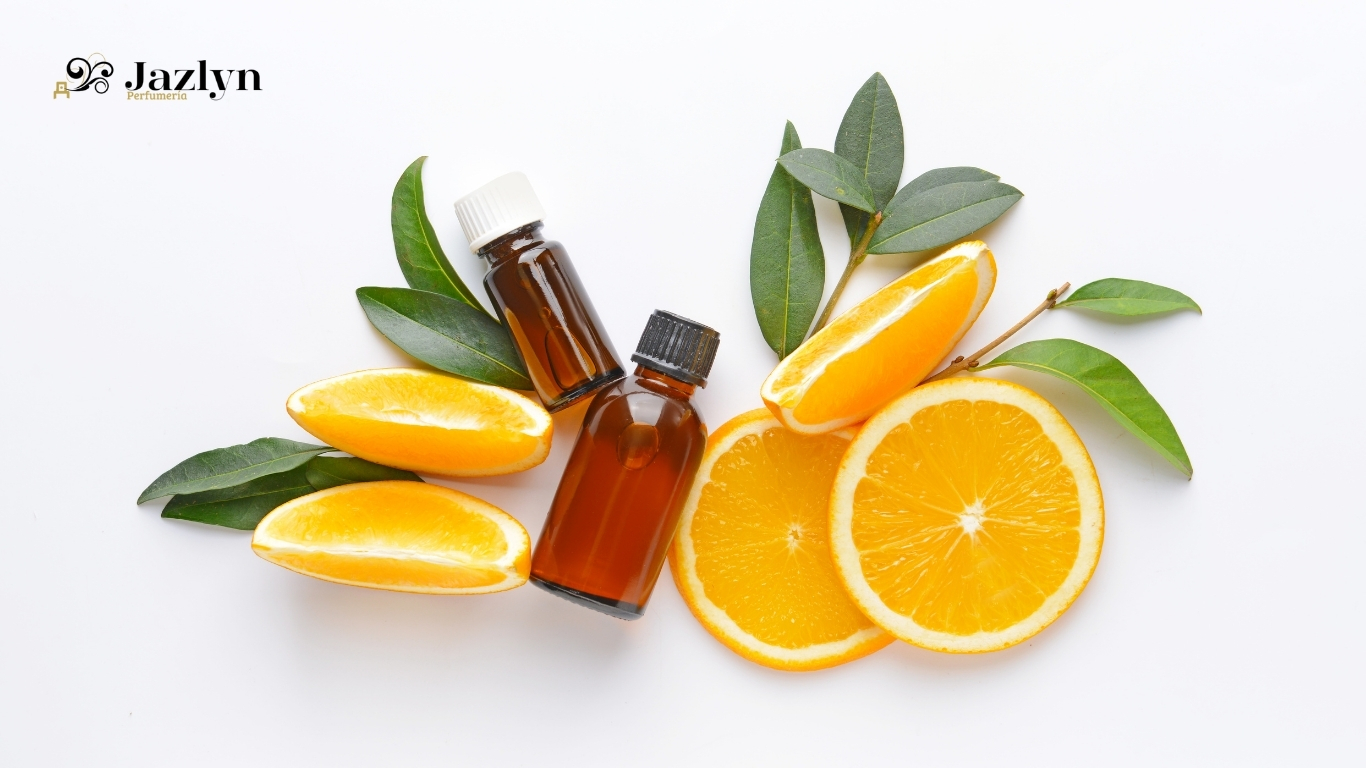 Botellas de aceites esenciales con rodajas y gajos de naranja sobre fondo blanco, aromaterapia cítrica natural de Jazlyn Perfumería.